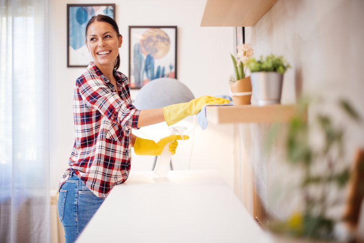 Young woman in casual clothes with yellow gloves cleaning furniture in living room at home.