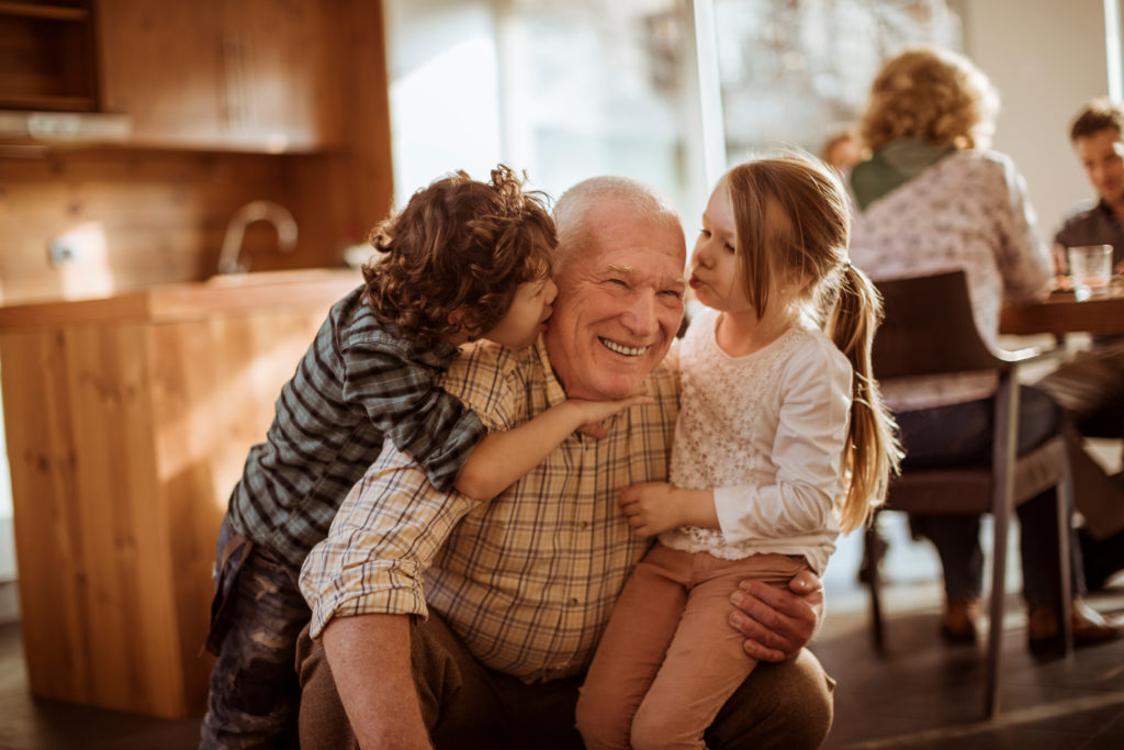 A grandfather hugs his small grandchildren